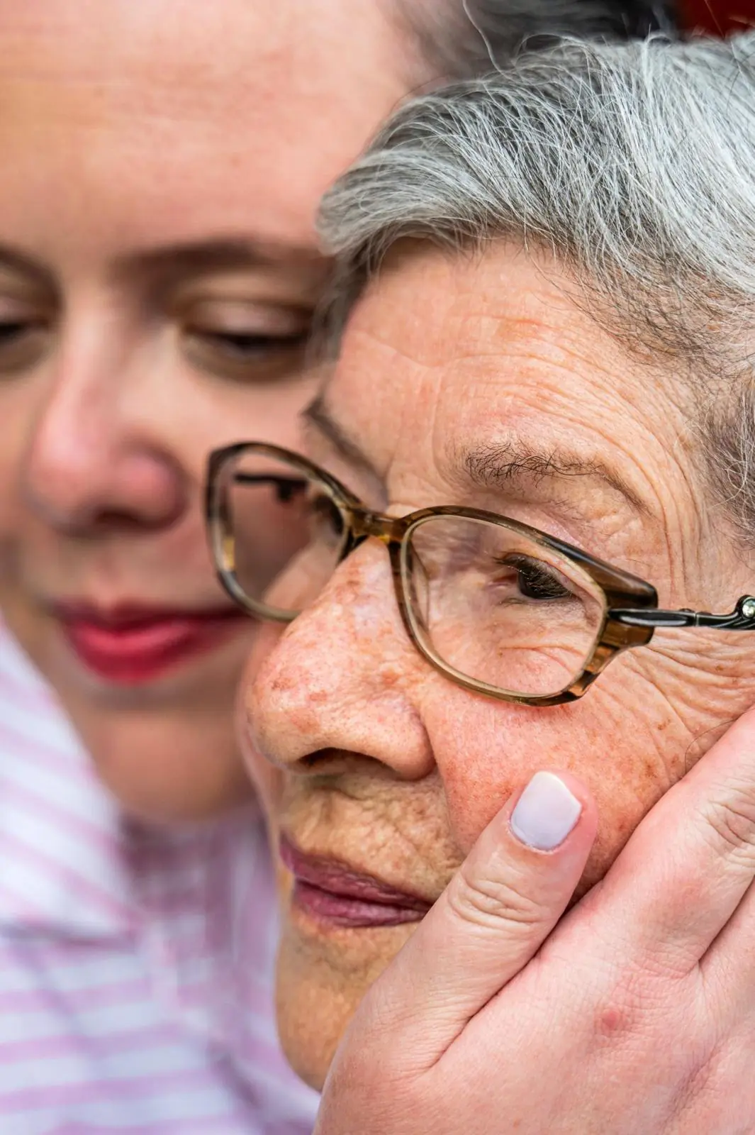 A caregiver hugging an older woman cheek to cheek